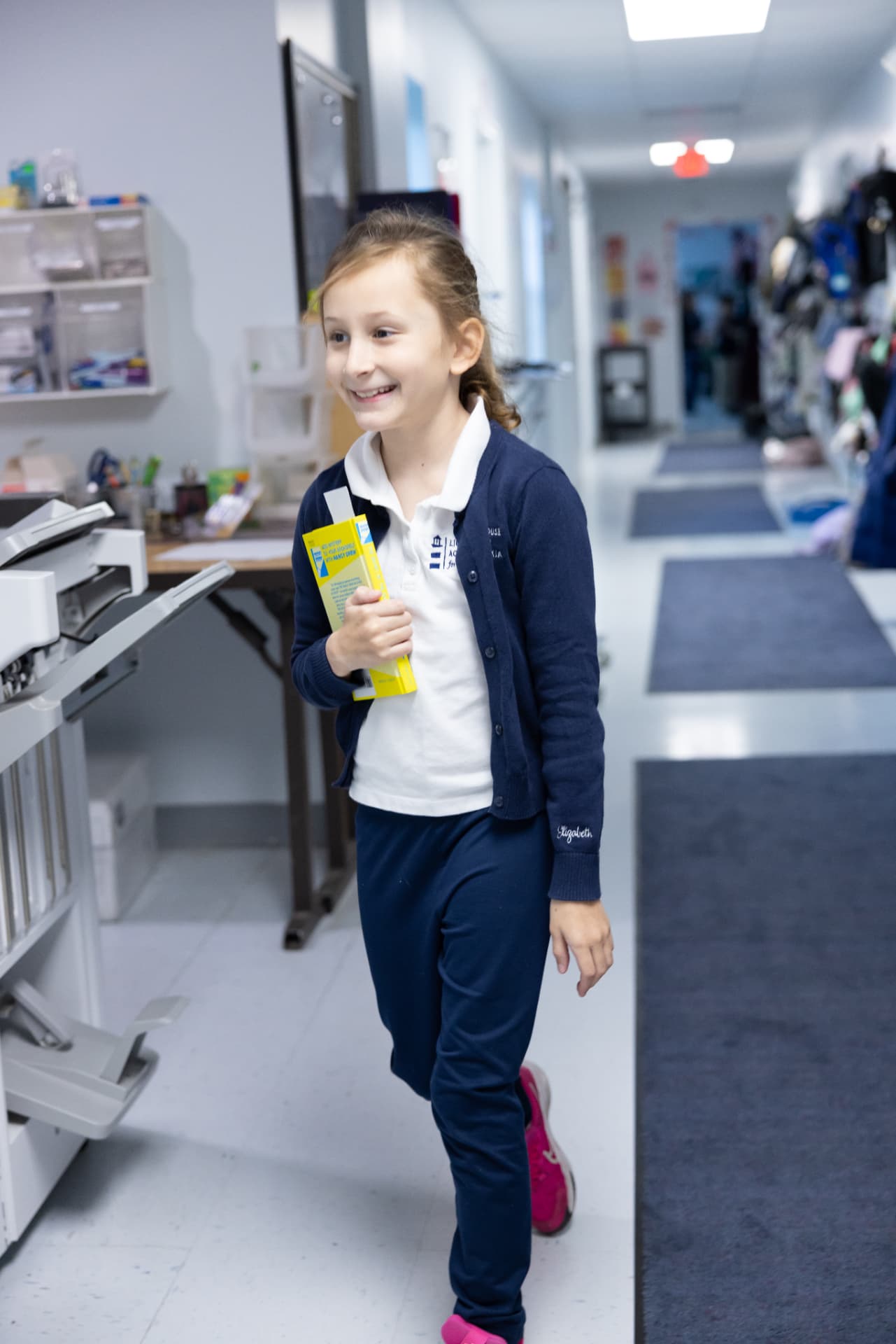 A smiling student walking down the hallway holding a library book