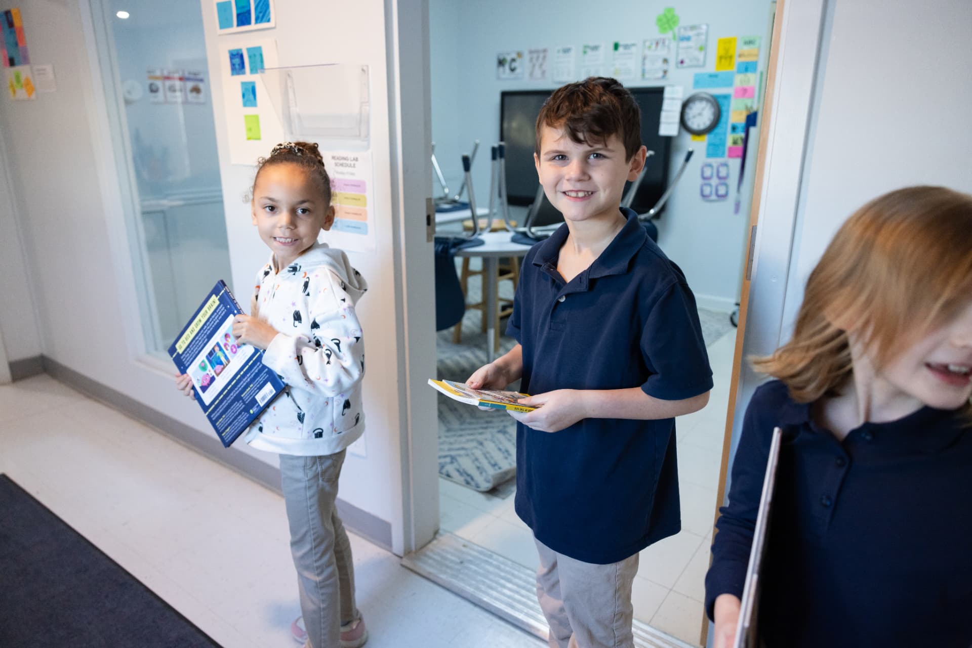 Two students smiling with library books in the reading lab doorway
