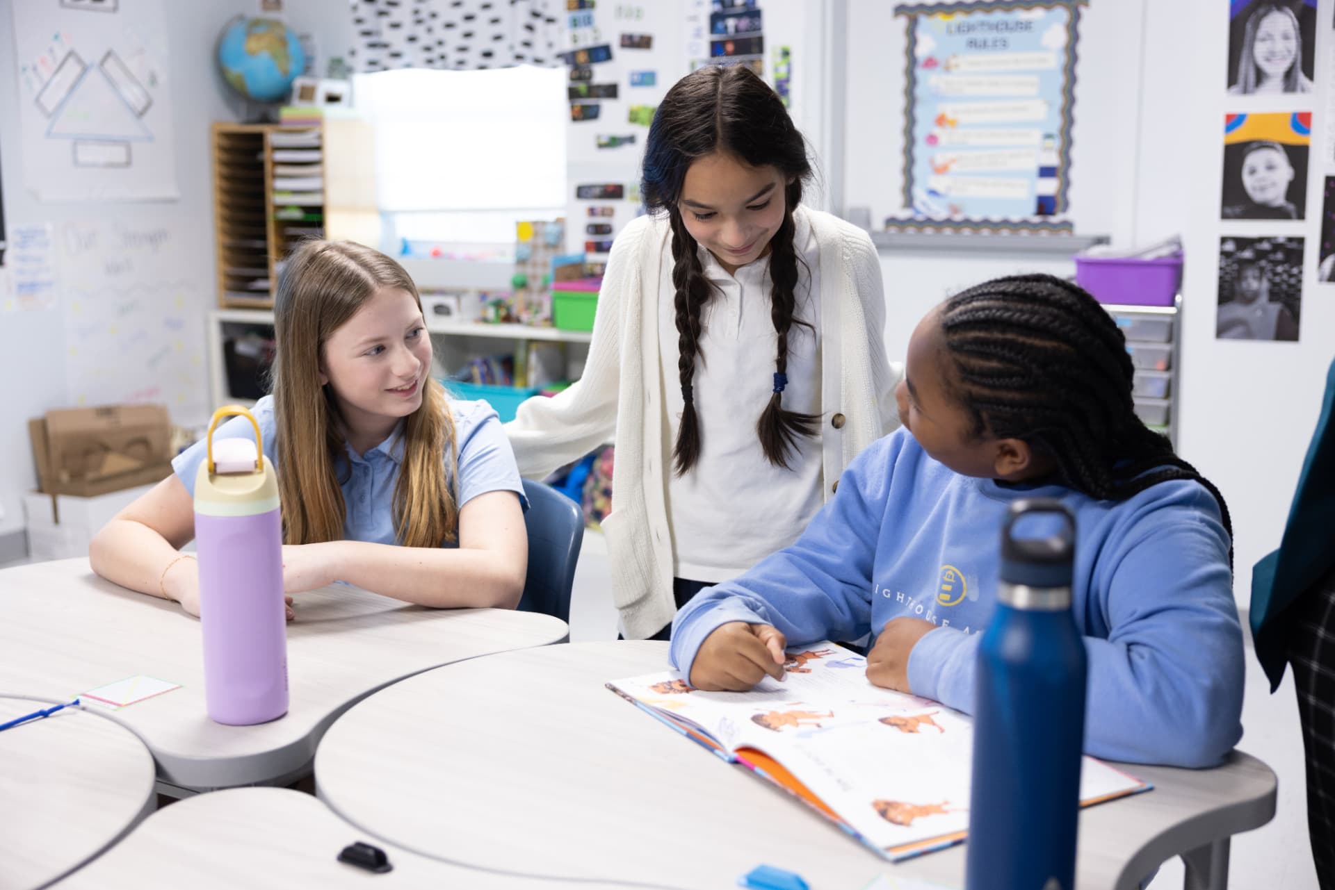Three students talking and laughing over an open book at their classroom tables