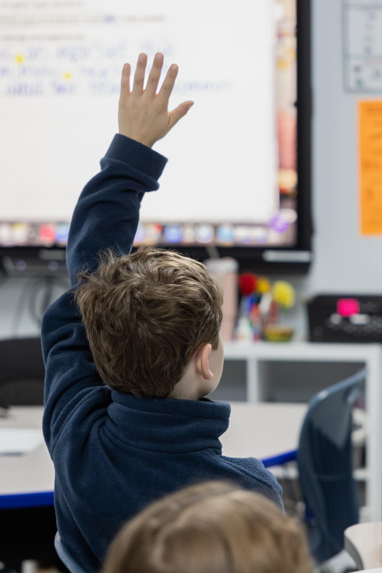 A student raising his hand toward the classroom board during a lesson