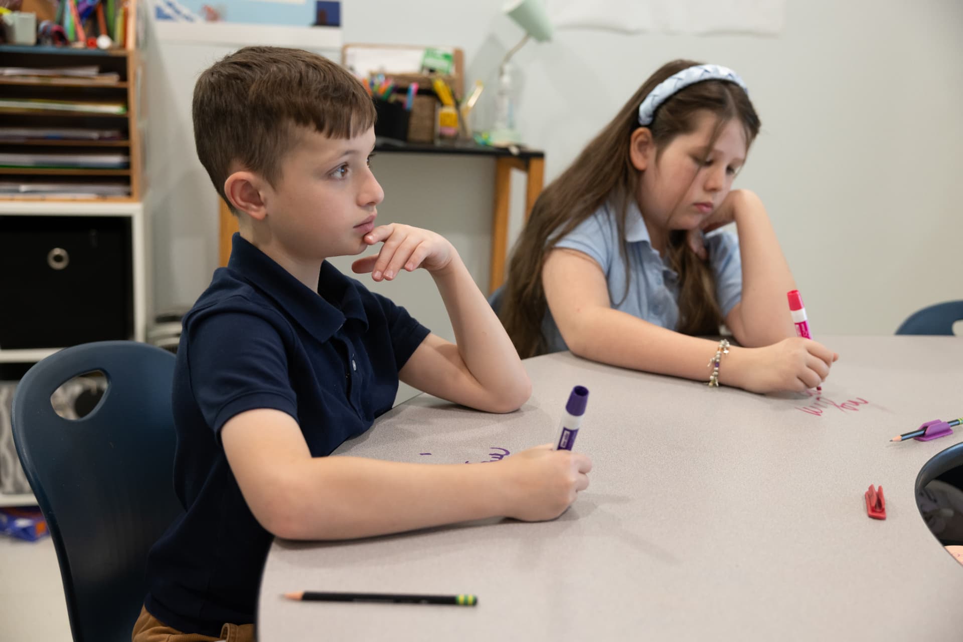 Two students writing directly on their whiteboard desktops during a spelling lesson