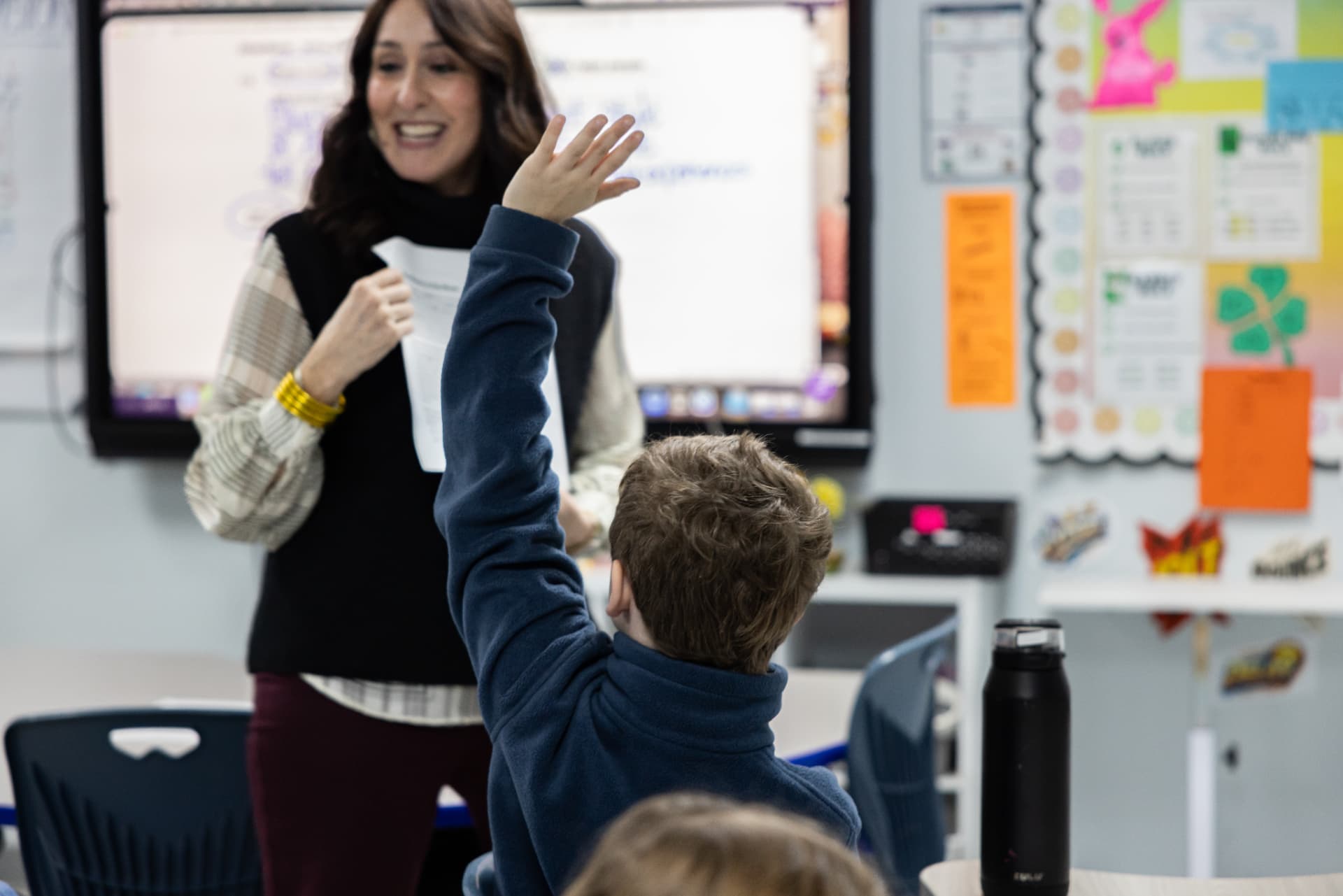 A smiling teacher calling on a student whose hand is raised high