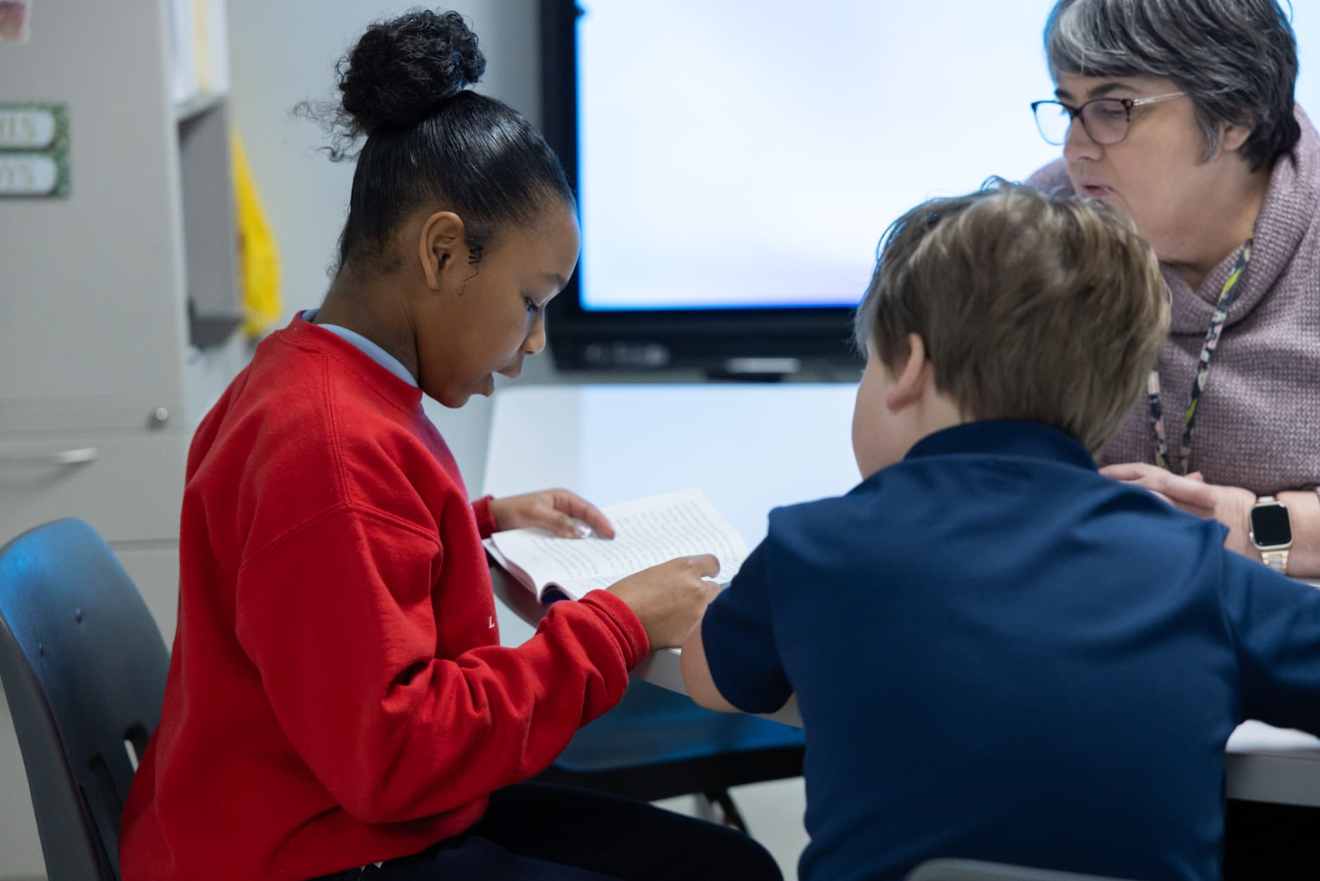 A dyslexia therapist guiding two students as they track words in a chapter book