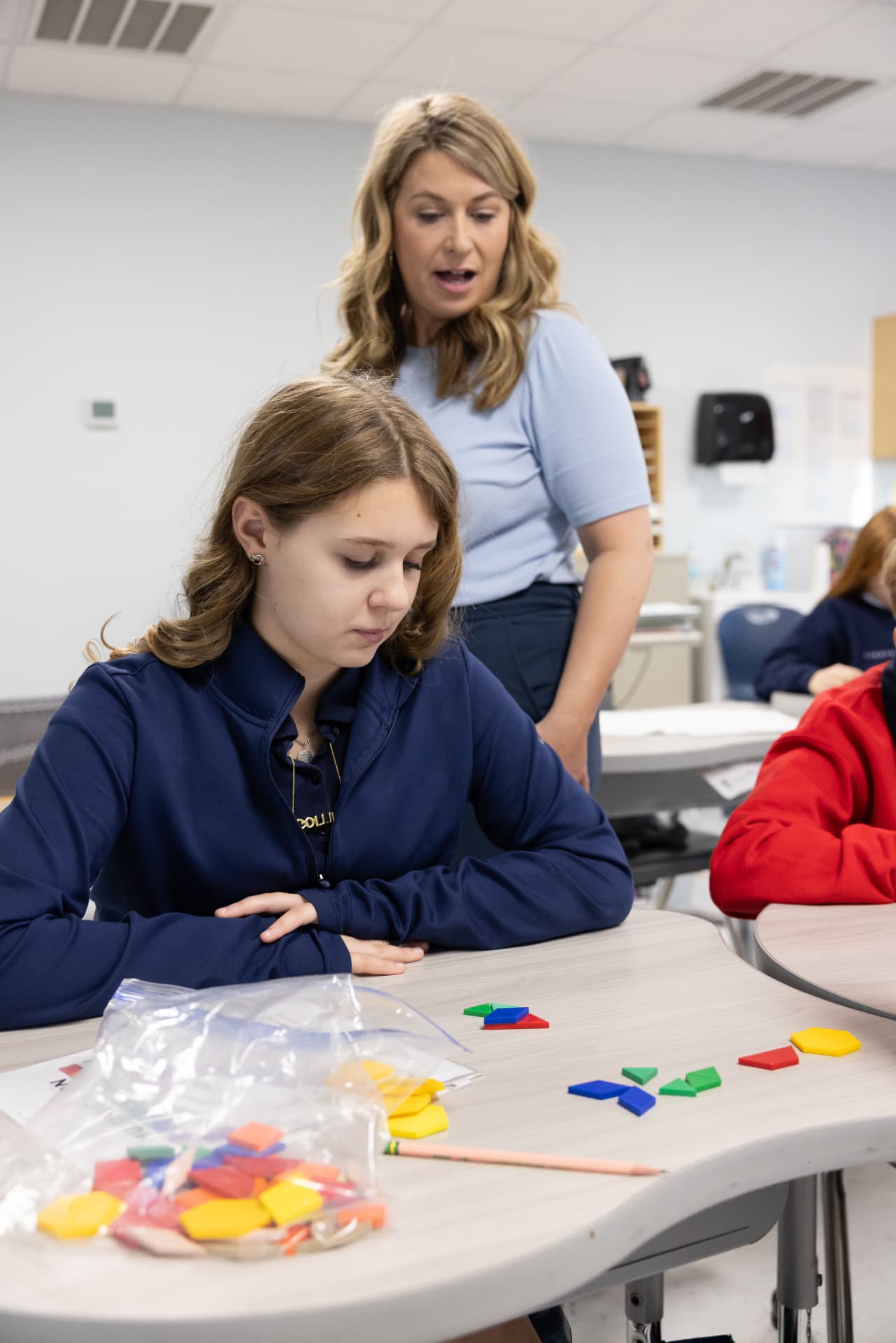 A teacher guiding a student working with colorful geometry manipulatives