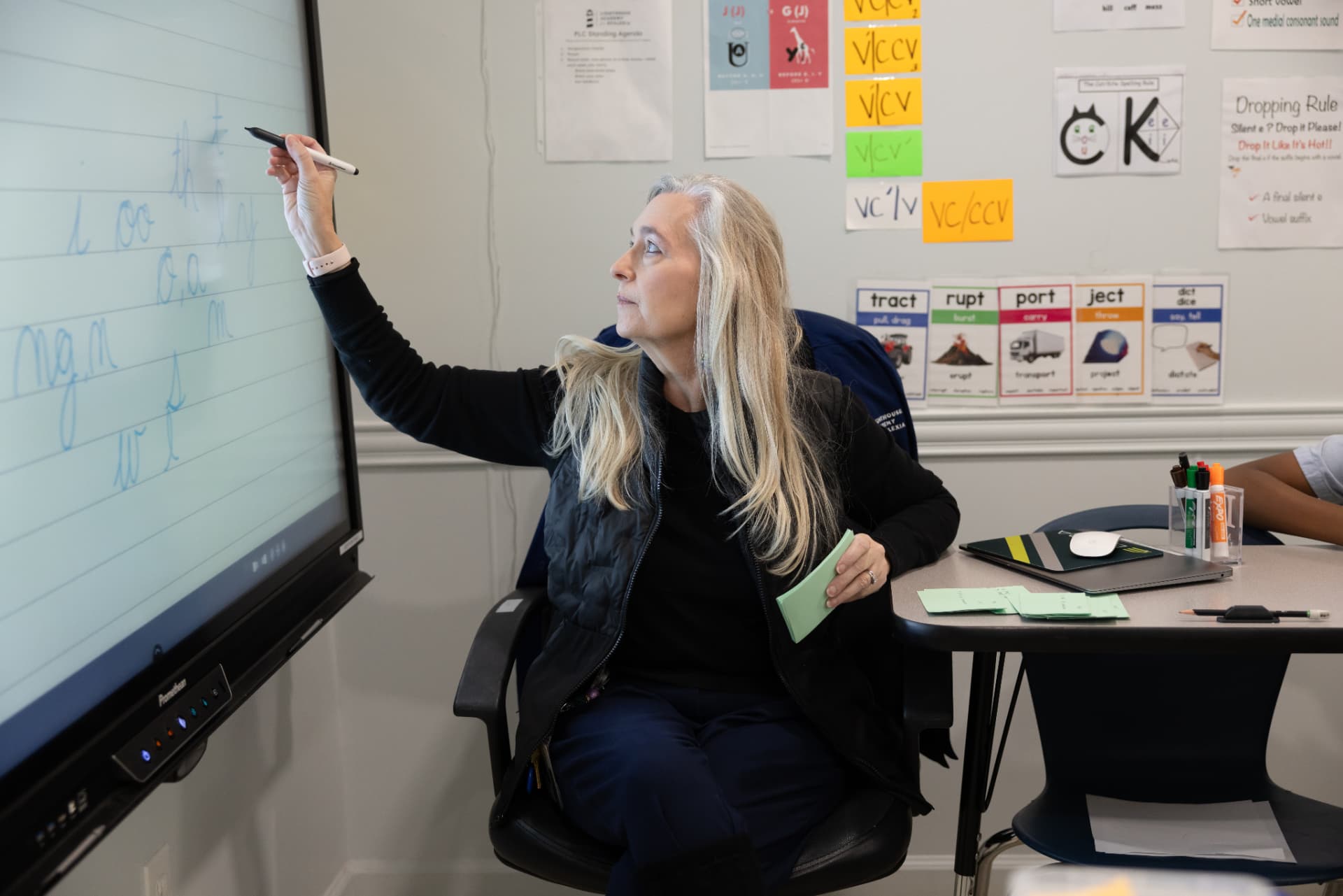 A dyslexia therapist modeling cursive letter formation on the classroom board