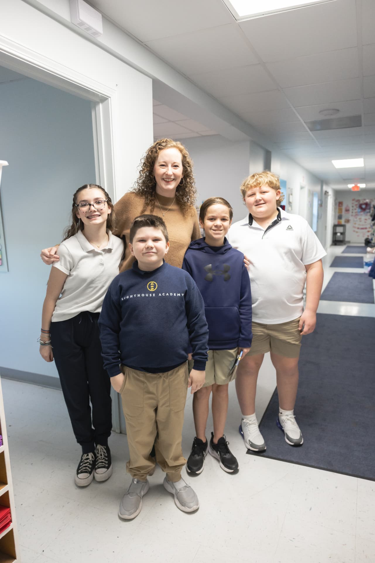 A teacher smiling in the hallway with four Lighthouse Academy students