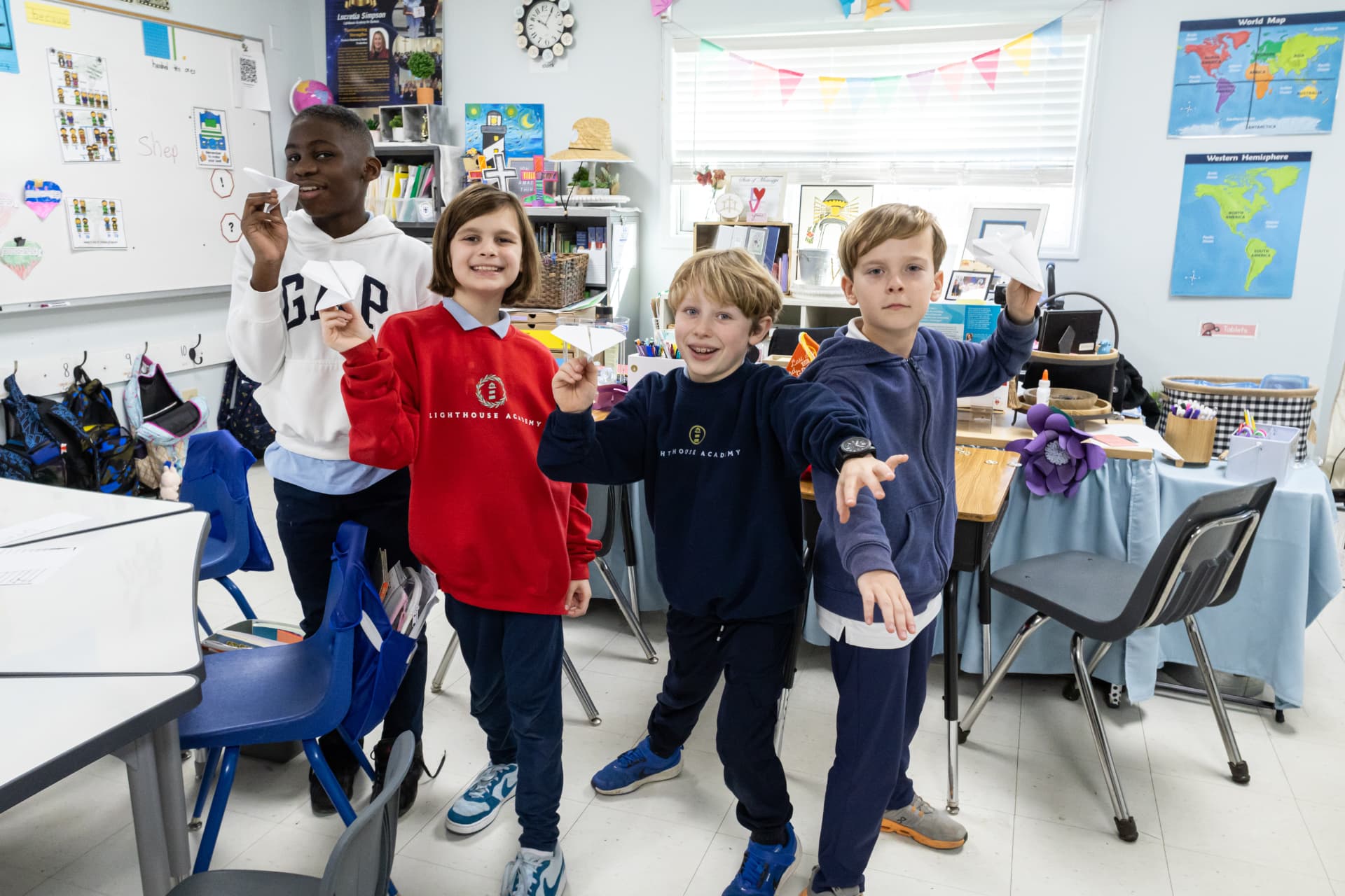 Four students grinning as they launch paper airplanes during a hands-on science lesson