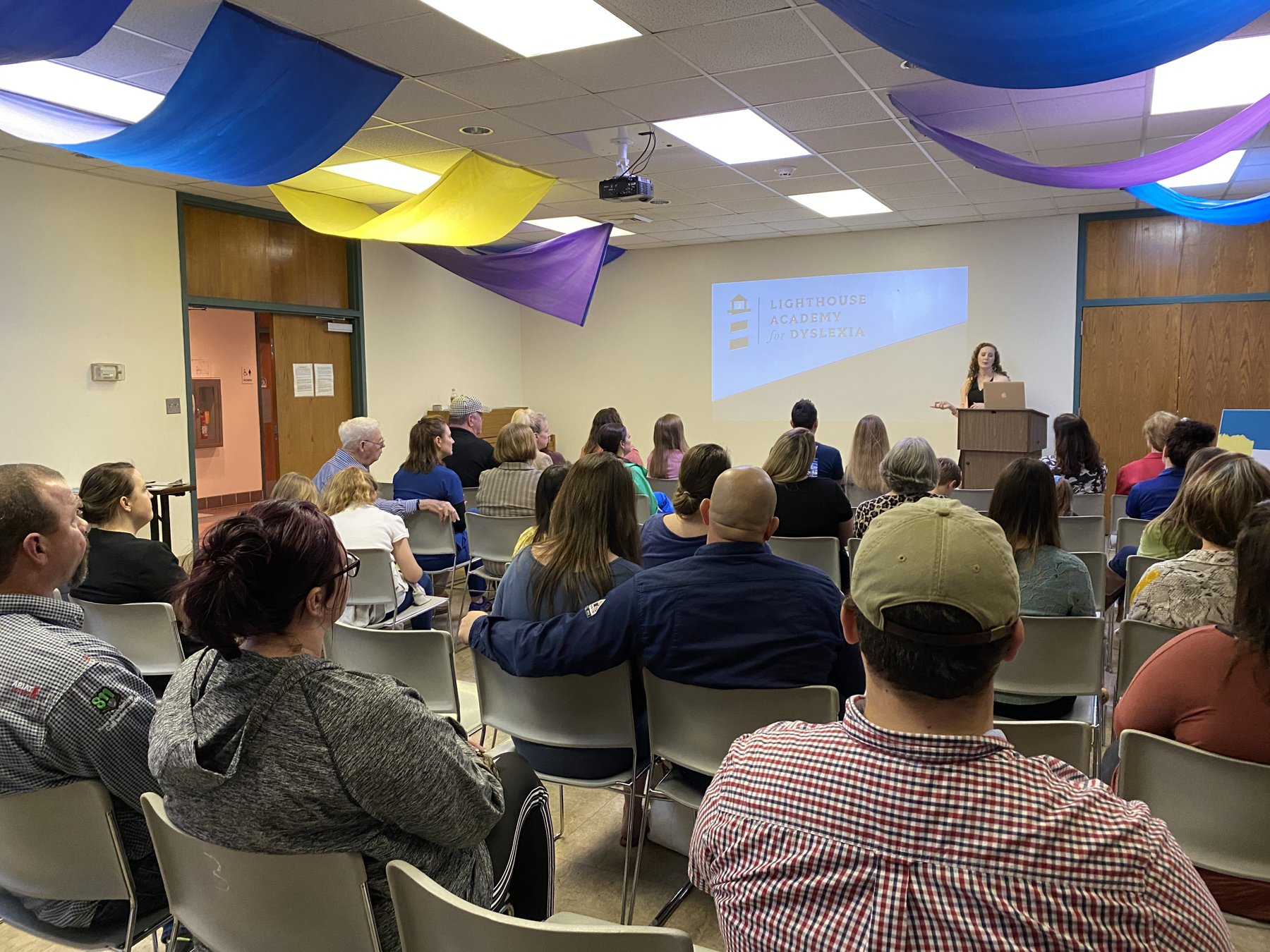 A packed community room at the Ocean Springs Library in February 2020, with the Lighthouse Academy for Dyslexia logo projected on the screen as a founder presents