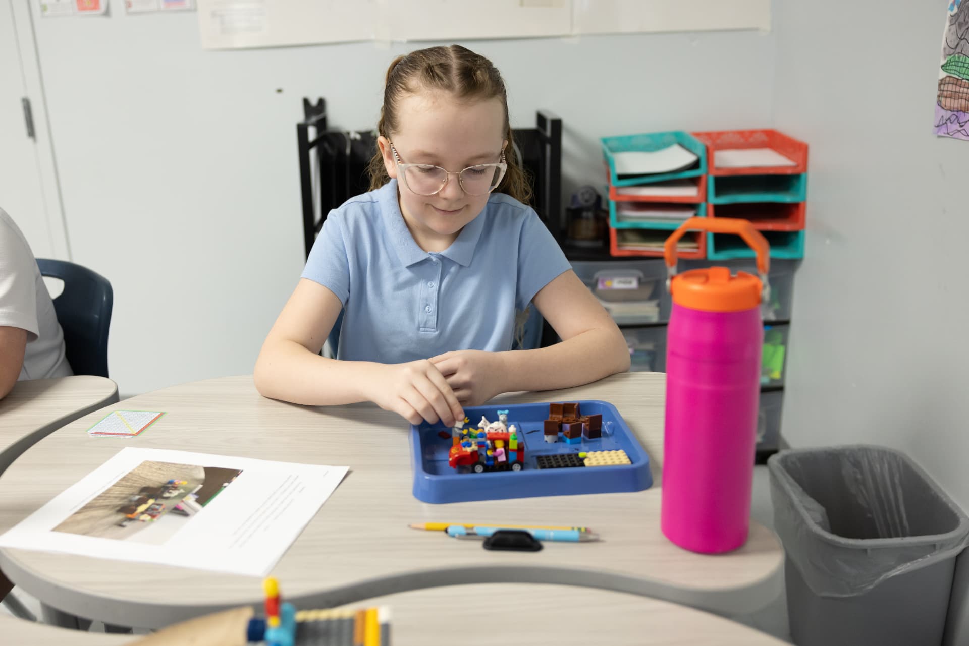 A student in glasses building a scene with small bricks at a hands-on work station