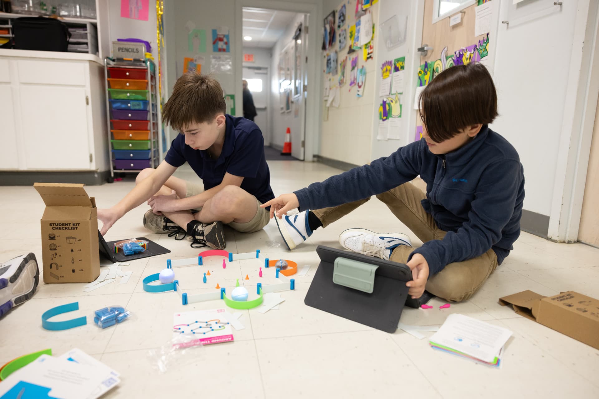 Two students building a robotics course on the floor with tablets