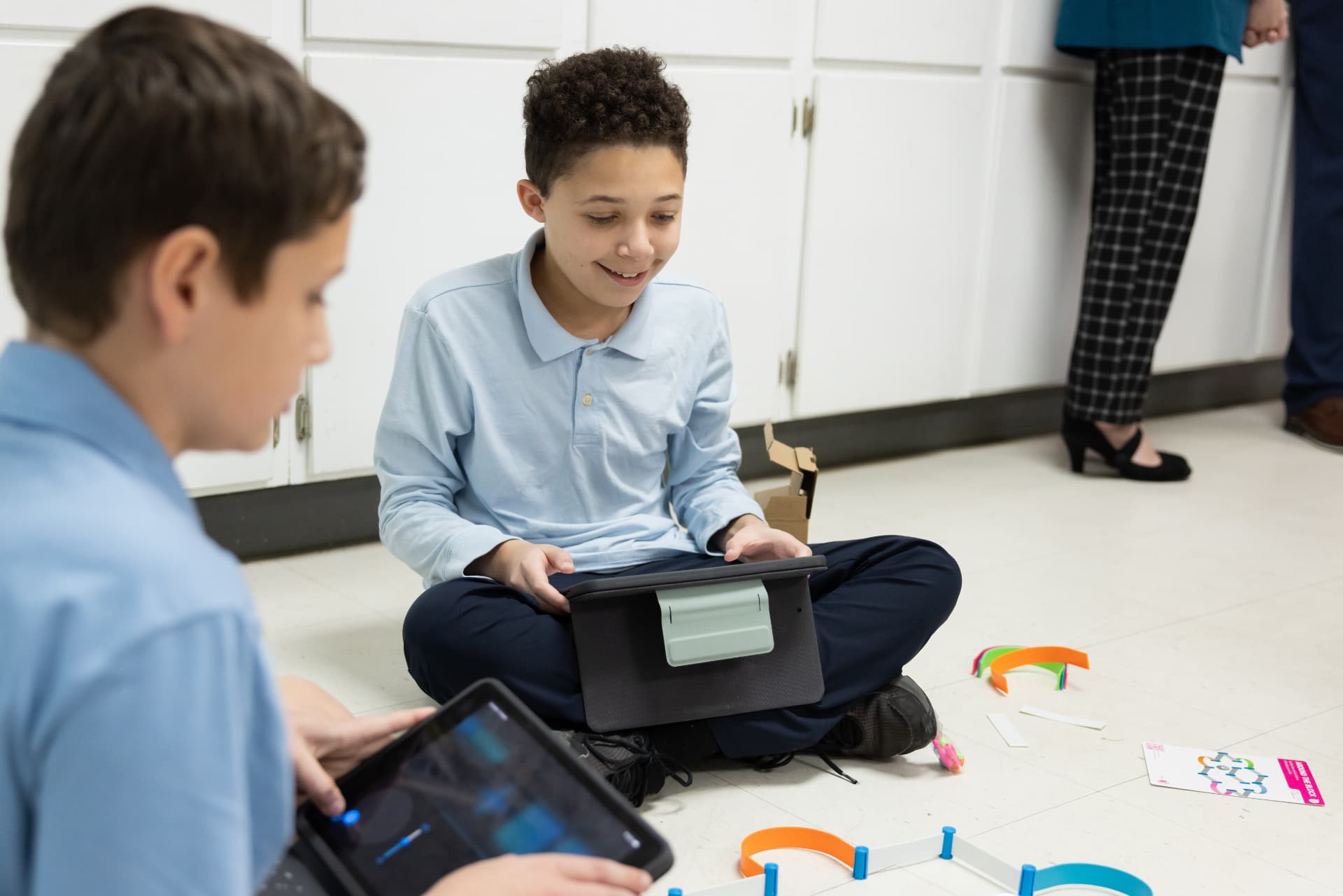 Two students smiling as they build a coding challenge on tablets on the classroom floor