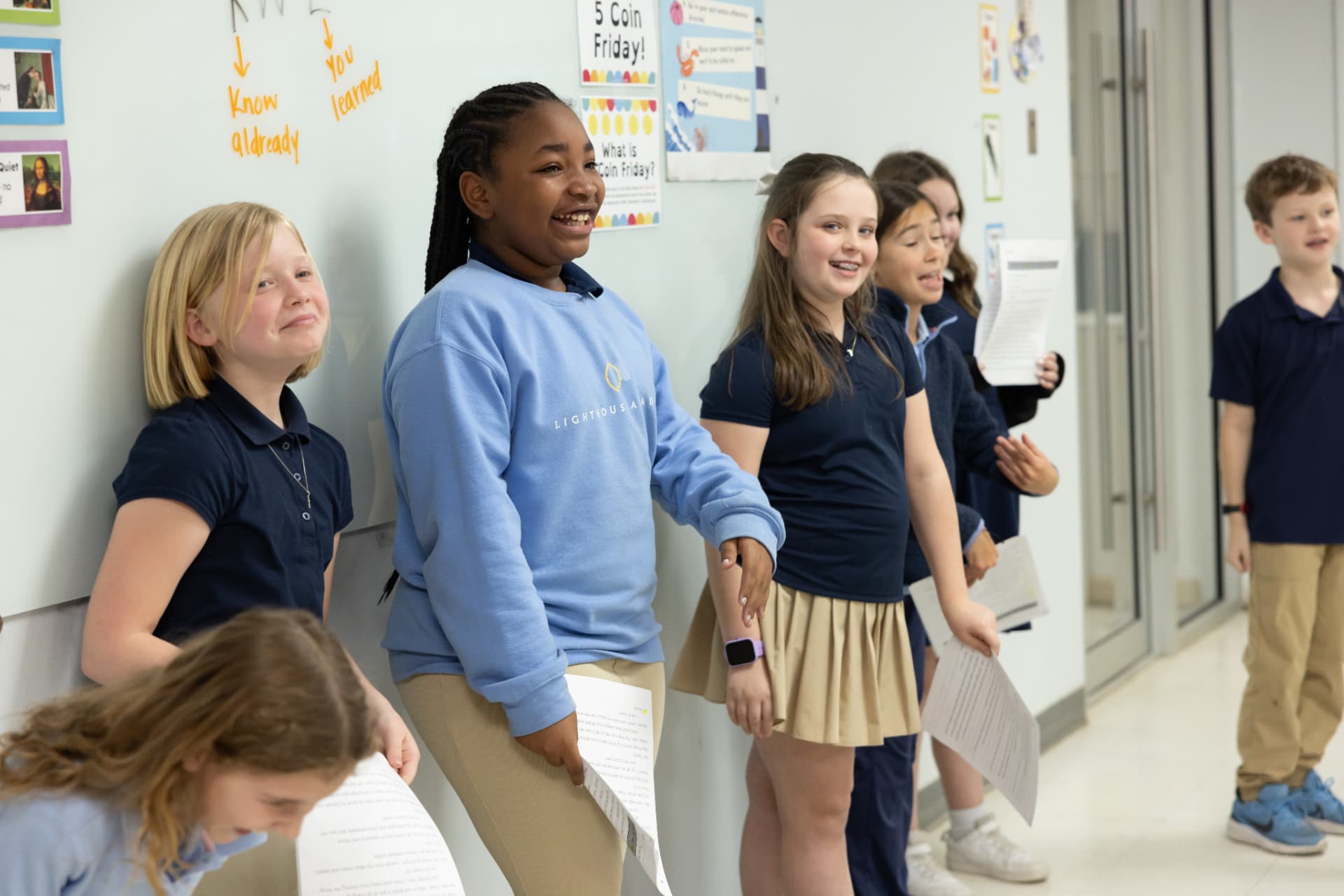 Students lined up in the hallway laughing while holding their reading passages