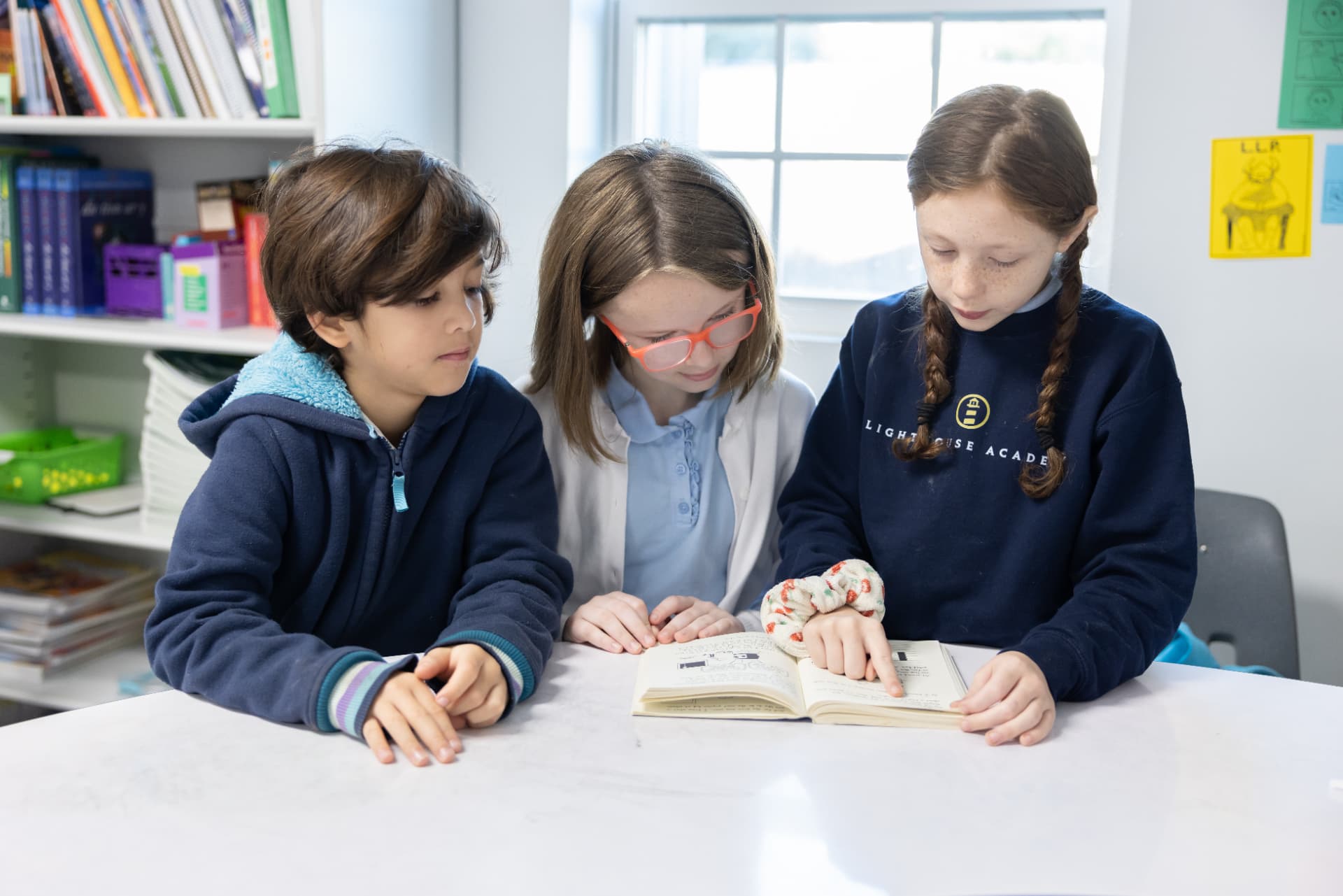 Three Lighthouse Academy students reading a chapter book together at a table